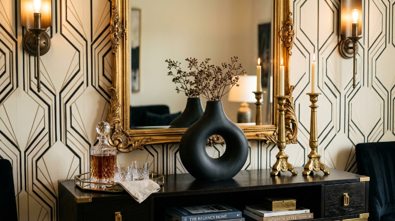 Black vase, gold candlesticks, and gilded mirror console table styling in a Hollywood Regency ideas living room.