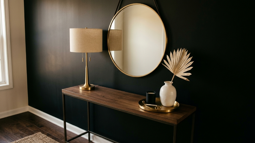 Brushed gold lamp and mirror styled on a black console table in a finished black and gold room